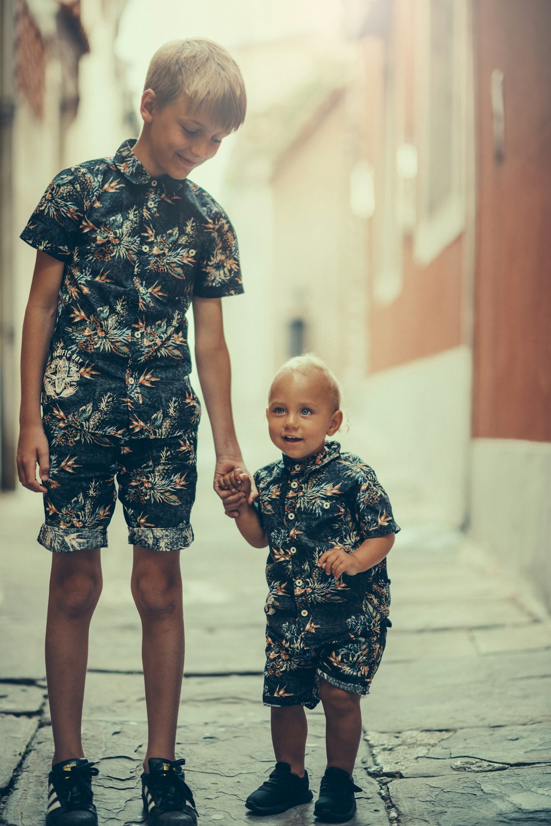 About matching-pair-of-boys-black-and-gray-floral-collared-shirt-and-shorts-standing-on-gray-concrete-area-pwcj9t7ne-q